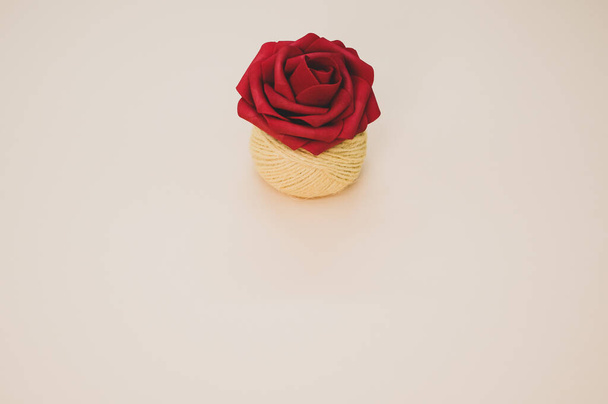 Un primo piano di una rosa rossa artificiale su una bobina di filo e una superficie di pesca pastello per uno spazio di copia - Foto, immagini