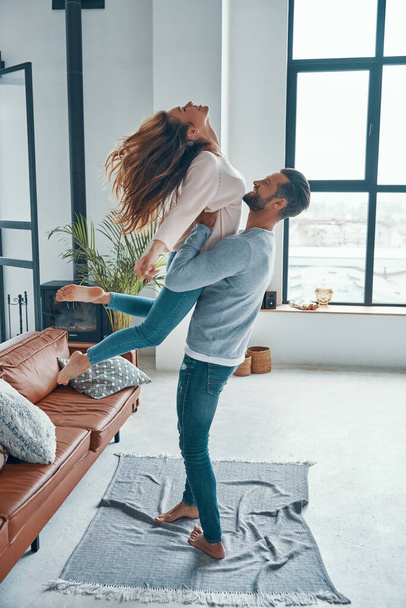 Full length of young playful couple smiling and dancing while bonding together at home - Foto, afbeelding
