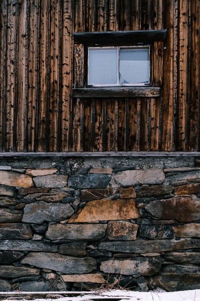 A vertical shot of a wooden building and a window with a stone wall on the foreground - Fotografie, Obrázek