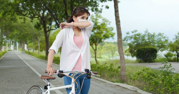 Asian sick female with protective mask coughing and riding bicycle in the park - Фото, изображение