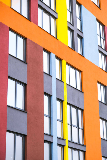 近代的な建物の角度と窓。多階建ての新しい多色のアパートの建物。フラットのスタイリッシュな生活ブロック。現代の住宅のファサードの一部。建物の建設に明るいジューシーな色. - 写真・画像