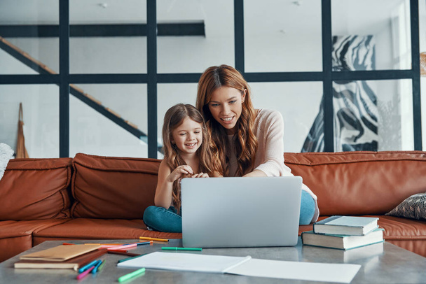 Young beautiful mother and her little daughter bonding together and smiling while using laptop at home - Fotoğraf, Görsel
