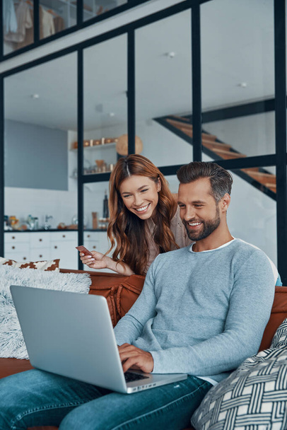Cheerful young couple using laptop and smiling while shopping online at home - Foto, Bild