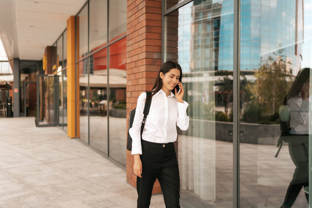 Nő üzleti hátizsák séta közben beszél telefonon közelében egy üzleti épület - Fotó, kép