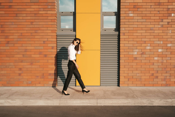 Şehir caddesinde güneş gözlüklü güzel bir kadın yürüyor. - Fotoğraf, Görsel