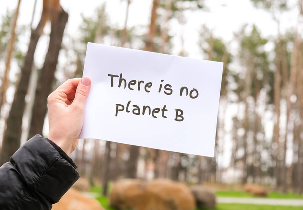 Female hands holding white paper sheet with text THERE IS NO PLANET B outdoors. Nature background. Protester activist. Lifestyle and activism - Фото, изображение