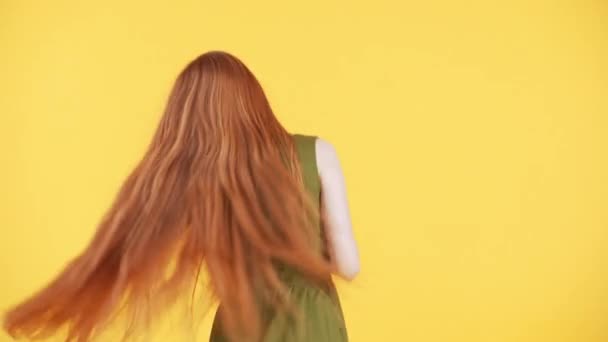 Espalda de una mujer con increíble pelo largo de jengibre bailando y moviendo su cabello sobre fondo amarillo. La mujer está bailando y disfrutando - Imágenes, Vídeo