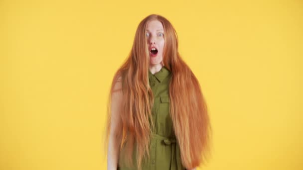 Çilli ve uzun kızıl saçlı genç bir kadın çerçevede beliriyor, sarı arka plandaki kameraya bakıyor. - Video, Çekim