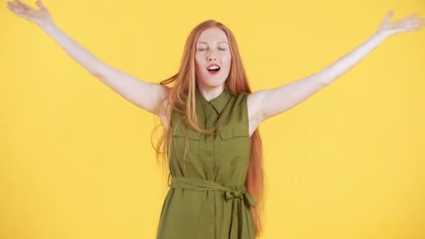 Une jeune femme avec des taches de rousseur et de longs cheveux roux apparaît dans le cadre, regardant dans la caméra et faisant un geste "chut" pointant quelque chose. Fond jaune - Séquence, vidéo