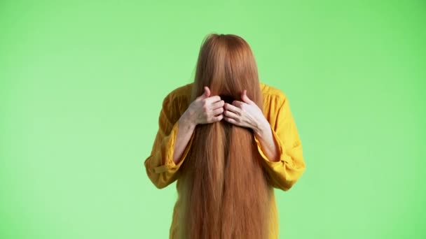 Woman is having her ginger hair on face, then looking through them into the camera, smiling and waving hand. Green background - Footage, Video