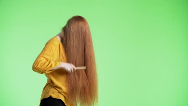 Jonge aantrekkelijke vrouw borstelt haar lange gember haar, gooit haar hoofd omhoog en kijkt glimlachend in de camera. Groene achtergrond - Video