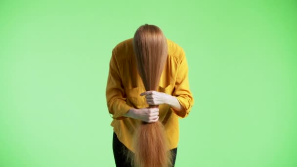 Woman is having her ginger hair on face, holding them, stroking and wounding them around the wrist. Green background - Footage, Video