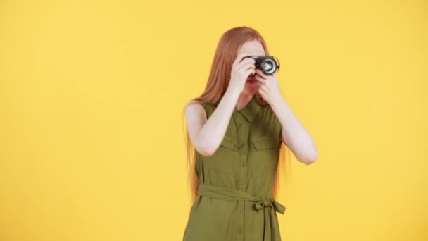 Mujer con el pelo largo de jengibre y la cámara en las manos está entrando en el marco y tomar fotos de todo lo que ve en el fondo amarillo - Metraje, vídeo
