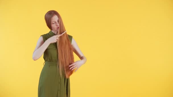 Młoda kobieta z piegami na twarzy delikatnie szczotkuje długie, piękne rude włosy i głaska je. Żółte tło - Materiał filmowy, wideo
