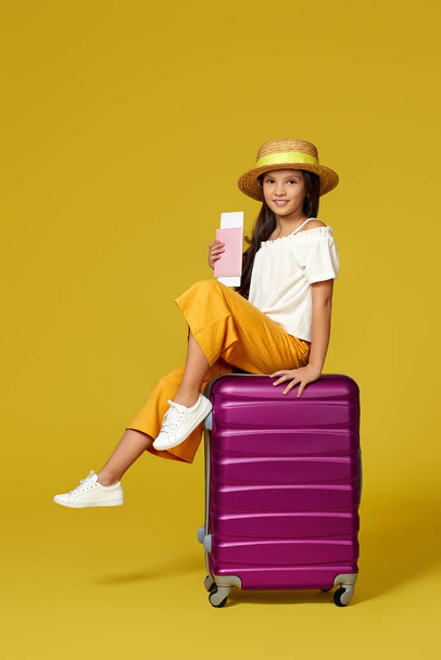 child girl in hat with passport and ticket sitting on suitcase - Foto, imagen