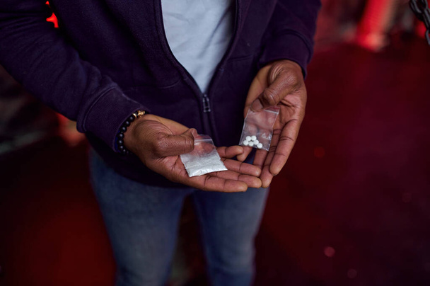 Наркоман держит в руках упаковку таблеток и порошка, на заднем плане размахивает интерьером, ден. Проблема наркомании, вечная депрессия наркоманов - Фото, изображение