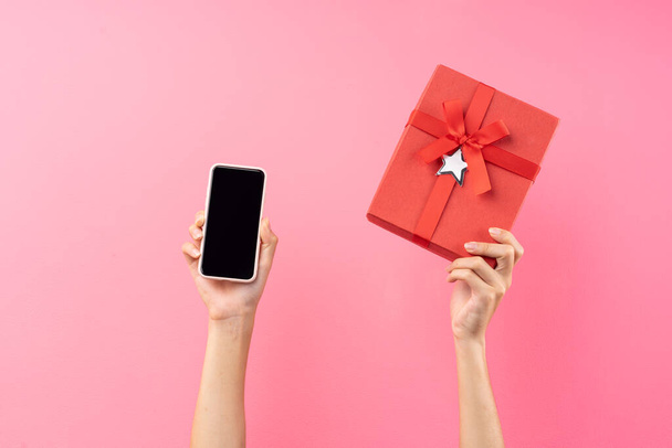 hands are holding red gift boxes and phones on a pink background - Zdjęcie, obraz