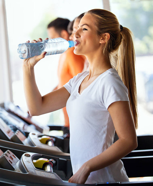 Happy young fit woman drinking during workout, running in the gym. Health, sport, people concept - 写真・画像