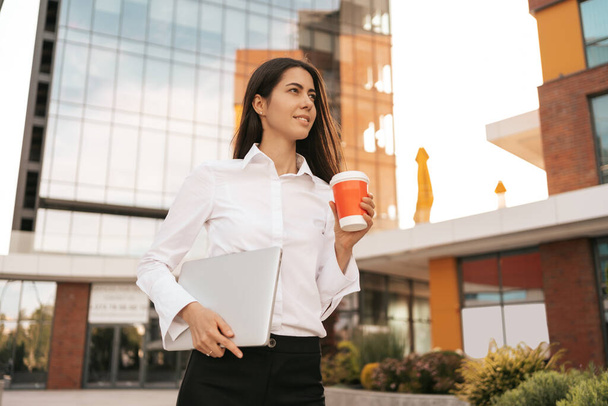 Millennial businesswoman talking on phone carrying a laptop - Photo, Image