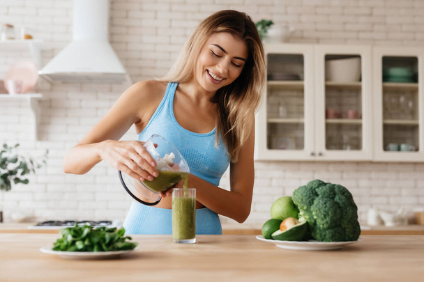 Blissful young woman smiling while puring yummy green smoothie into a glass - Photo, image