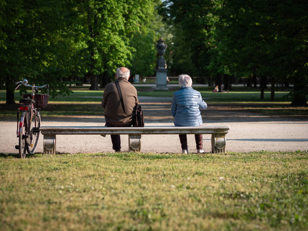 Um homem e uma mulher idosos sentados muito separados em um banco em um parque público. - Foto, Imagem