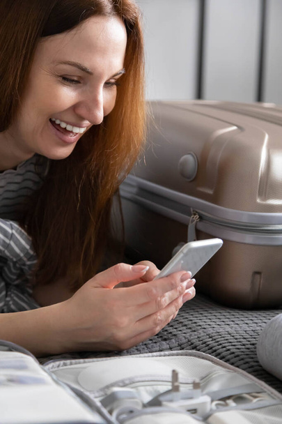 Woman chatting surfing internet use smartphone application during packing suitcase baggage - Zdjęcie, obraz