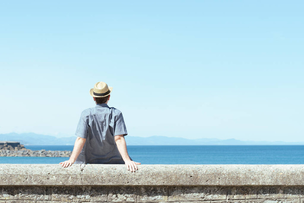 Hombre solitario sentado hacia atrás y mirando al horizonte a la orilla del mar en un soleado día de verano. - Foto, Imagen