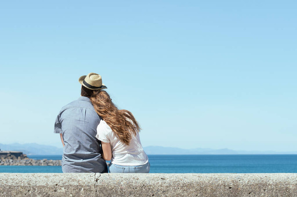Paar achterover zittend kijkend naar de horizon aan de kust in een zonnige dag. - Foto, afbeelding