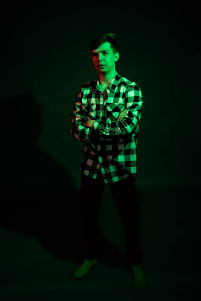 Portrait of a guy in a plaid shirt with red and green light on a black background - Foto, afbeelding