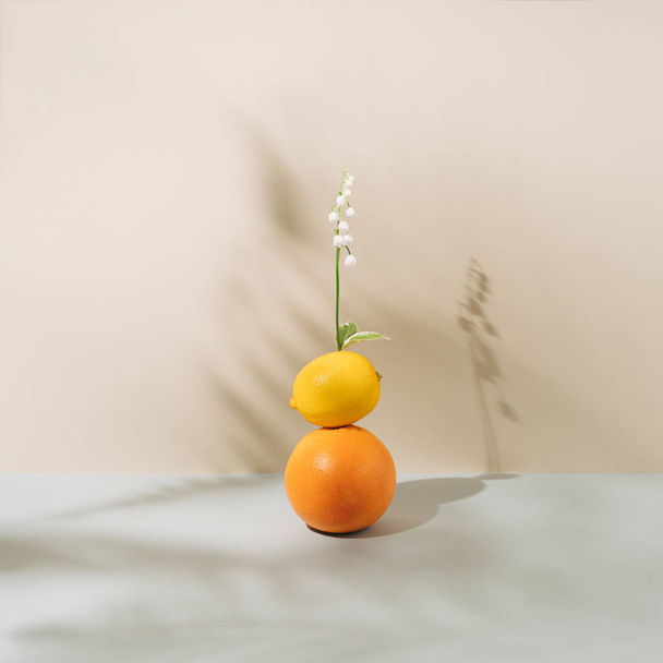Vibrant orange, yellow lemon and white lily of the valley on biege wall. Spring or summer pastel background with shadows. Minimal concept art. - Foto, imagen