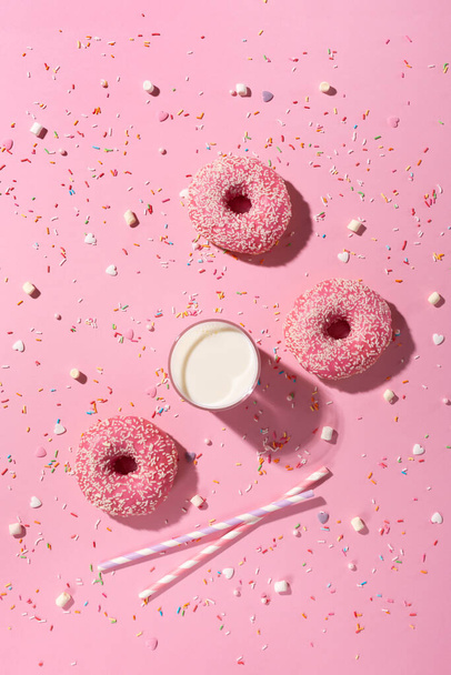 Happy National Donut Day koncept. Koblihy s růžovou polevou, sklenicí mléka a cukrem posypané růžovým pozadím. Horní pohled, kopírovací prostor. - Fotografie, Obrázek