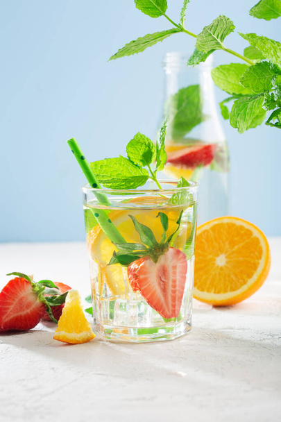 Fresh fruit flavored water with strawberry, lemon, mint. Blue sun background, copy space. Summer drink concept. Detox fruit infused water. - Photo, Image