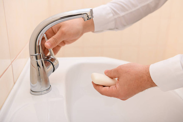 handwas met zeep of gel onder stromend water in de wastafel, reinheid en hygiëne, mannenhanden gekleed in een wit hemd - Foto, afbeelding