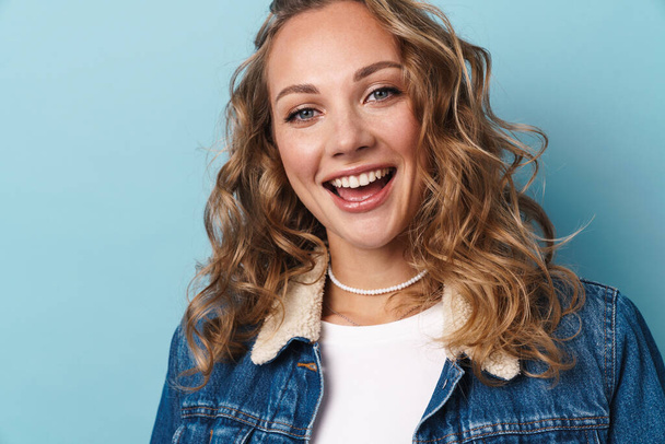 Blonde happy woman smiling and looking at camera isolated over blue wall - Foto, afbeelding