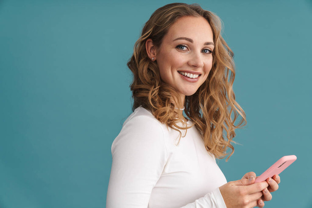 Blonde happy woman using mobile phone and smiling isolated over blue wall - Photo, Image