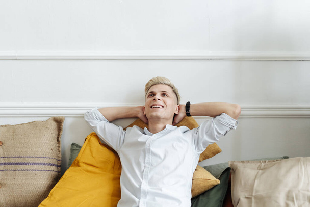 Smiling casual guy relaxing and daydreaming on sofa at home. - Photo, Image