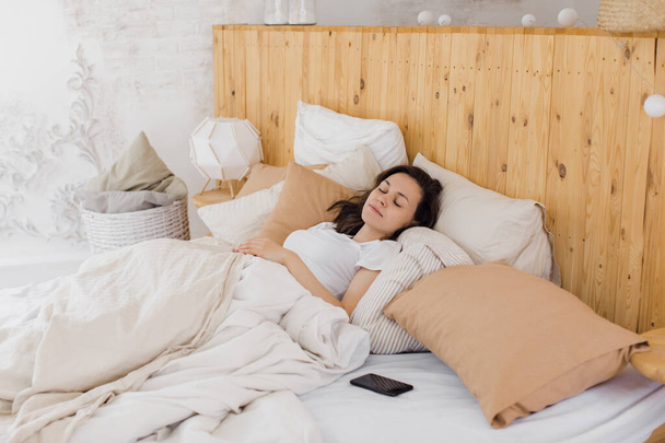 An attractive girl sleeps in a bed in her modern bright apartment - Foto, afbeelding