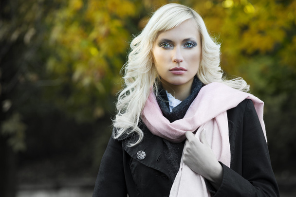 close up fashion portrait of a blond girl with hair style in black coat and pink scarf with forest in background - Фото, изображение