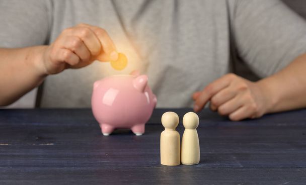 wooden figurines of little men family on the background of a man with a piggy bank. The concept of savings and long-term budgeting, cost savings. Cash back from purchases, benefit - Photo, Image