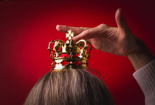Frau mit langen blonden Haaren hält goldene Krone auf dem Kopf. - Foto, Bild