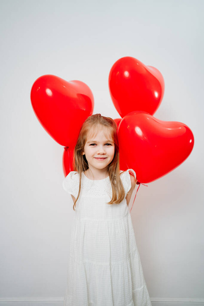 Funny little girl with red balloons smiling near white wall - Foto, Imagem