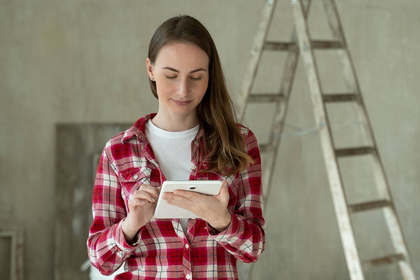 Young woman stand in new apartment, using tablet, choosing new design of house. Home repair - Φωτογραφία, εικόνα