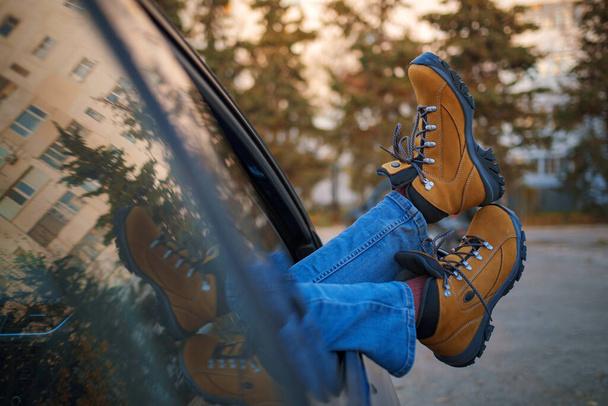 Frauenfüße in trendigen gelben Wanderschuhen an der Autotür. Füße vor dem Fenster im Wald bei Sonnenuntergang. Das Konzept der Bewegungsfreiheit. Ein Herbstwochenende in der Natur. - Foto, Bild