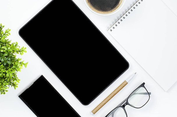 tablet, smartphone, notebook, tazza da caffè, fiore, penna e occhiali su tavolo bianco - Foto, immagini