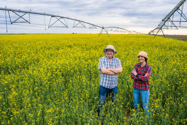 Proud two generations farmers are standing in their rapeseed field. - Fotó, kép
