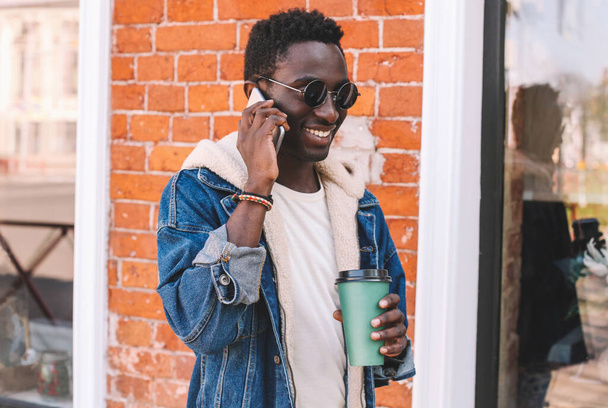 Portrait of happy smiling african man talking on smartphone on a city street - Fotó, kép