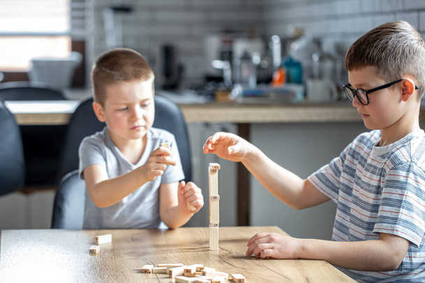 Μικρά παιδιά παίζουν ένα επιτραπέζιο παιχνίδι με ξύλινα κύβους στο σπίτι στην κουζίνα. - Φωτογραφία, εικόνα