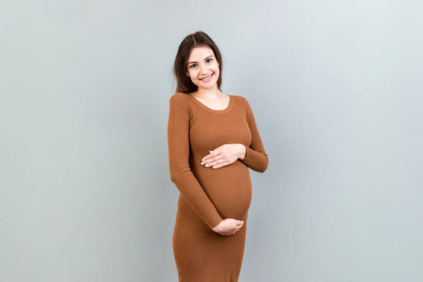 Happy pregnant woman touching her abdomen at Colored background. Future mother. Expecting of a baby. Copy space. - Fotó, kép