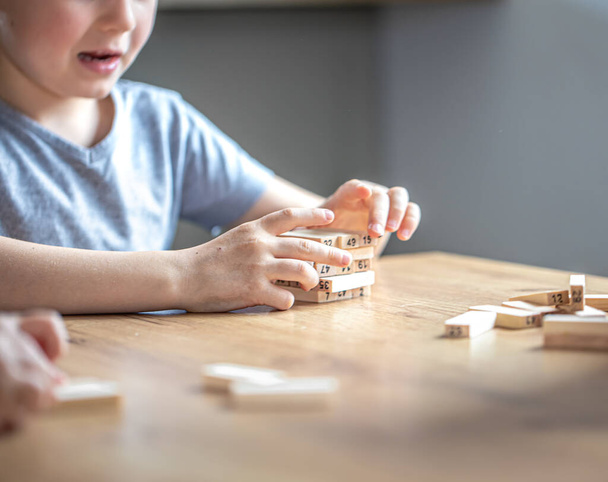 Küçük tatlı bir çocuk tahta küpleri ve tareti olan bir masa oyunu oynuyor.. - Fotoğraf, Görsel