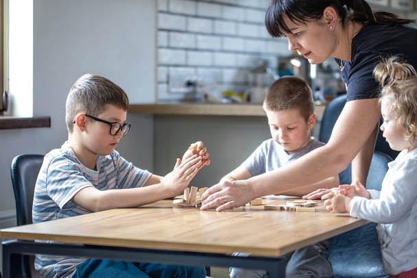 Pienet lapset leikkivät lautapeliä puisilla kuutioilla kotona keittiössä äidin kanssa.. - Valokuva, kuva